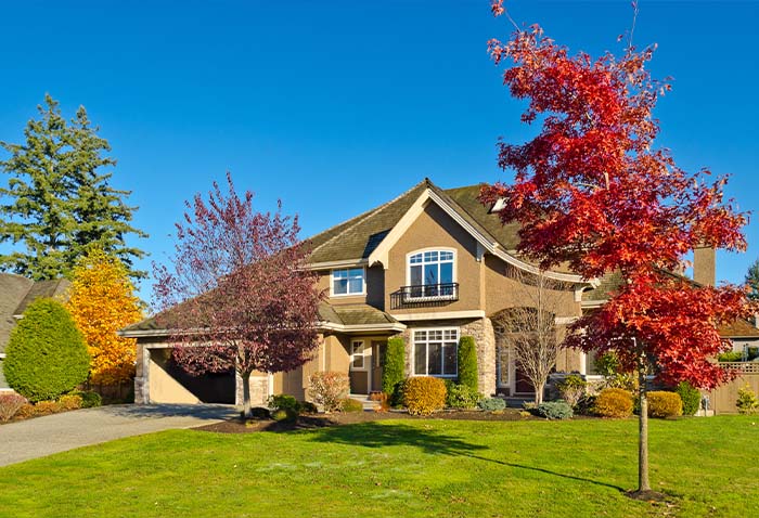 A two-story suburban house with a landscaped front lawn and colorful autumn trees under a clear blue sky. A two-story suburban house with a landscaped front lawn and colorful autumn trees under a clear blue sky.